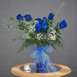 Blue roses in a glass vase with white baby's breath and a blue ribbon