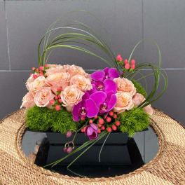 Peach roses and purple orchids in a low black container