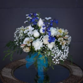 White and blue floral arrangement in a glass vase with a blue ribbon