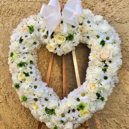 Heart-shaped white floral wreath with a ribbon bow on an easel