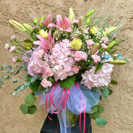 Pink and yellow mixed bouquet with lilies, roses, and hydrangeas in a glass vase