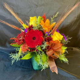 Bright mixed bouquet in a teal vase with a brown ribbon
