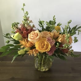 Mixed bouquet of peach, yellow, and pink flowers in a glass vase