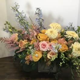Mixed bouquet of roses, dahlias, and blue delphinium in a low container
