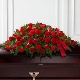 Red rose casket spray with a red ribbon on a dark casket