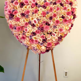 Heart-shaped rose arrangement on an easel in pink, peach, and purple tones