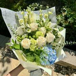 Bouquet of white roses, blue hydrangea, and green accents wrapped in paper