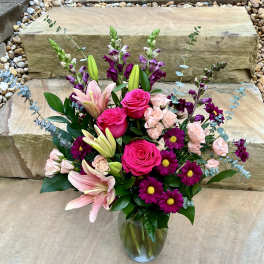 Bouquet of pink roses, lilies, and purple daisies in a glass vase