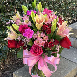 Bouquet of pink and red roses with lilies in a glass vase and pink ribbon