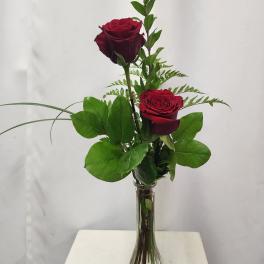 Two red roses in a clear glass vase with greenery