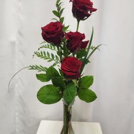 Four red roses in a clear glass vase with greenery