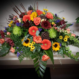 Large colorful floral casket spray with roses, gerbera daisies, and sunflowers