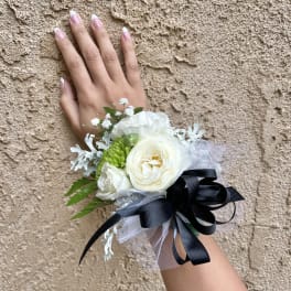 White floral wrist corsage with black ribbon on a hand