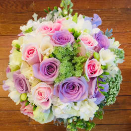 Round bouquet of pink, lavender, and white roses with small white flowers