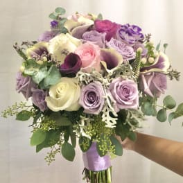 Handheld bouquet of pastel roses and calla lilies with greenery