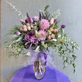 Mixed pink and purple bouquet in a clear glass vase with trailing greenery