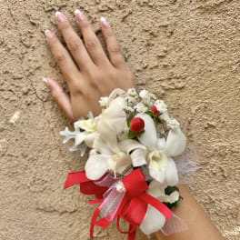 White floral wrist corsage with red ribbon on a hand