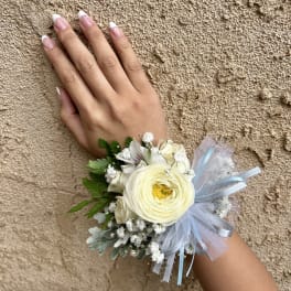 White floral wrist corsage with blue ribbon on a hand