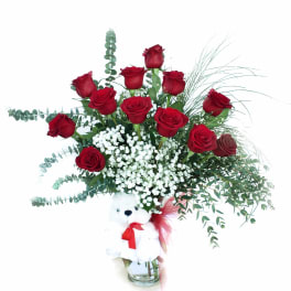 Red roses in a glass vase with a teddy bear attached