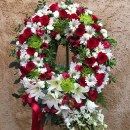 Circular wreath of red roses, white daisies, and lilies with a red ribbon