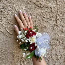 Hand wearing a floral wrist corsage with red and white roses