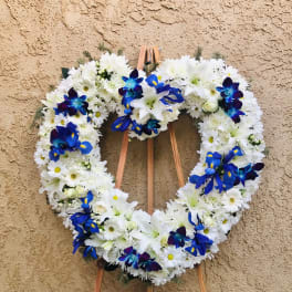 Heart-shaped white floral wreath with blue accent flowers on a wooden easel