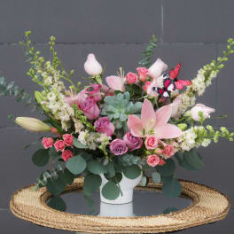 Pink and white floral arrangement in a white vase with butterfly accents