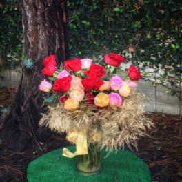 Bouquet of red, pink, and peach roses in a glass vase with a gold ribbon
