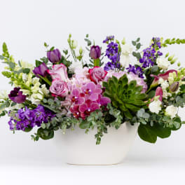 Mixed purple and white floral arrangement in a white bowl vase