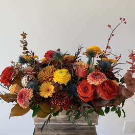 Mixed bouquet of red, yellow, and peach flowers in a wooden container