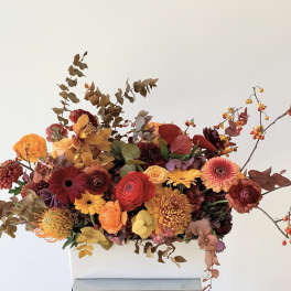Autumn floral arrangement in a white rectangular vase with orange, red, and yellow blooms