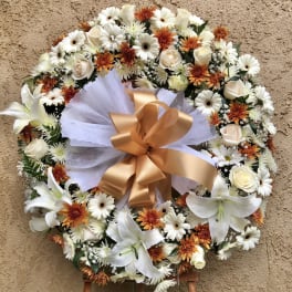 Round floral wreath with white lilies, daisies, and orange blooms on an easel
