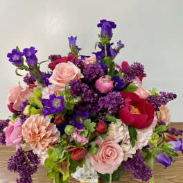 Mixed bouquet of pink, purple, and red flowers in a white vase