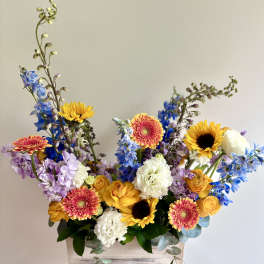 Mixed bouquet in a wooden box with sunflowers, gerbera daisies, and blue flowers