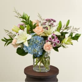Mixed bouquet in a clear glass vase with blue hydrangea, white lilies, and peach roses