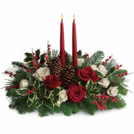 Christmas centerpiece with red and white roses, evergreens, red berries, pine cones, and two red taper candles