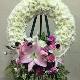 White floral wreath on an easel with pink lilies and roses at the base