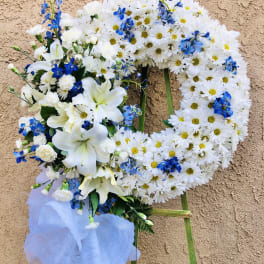 White daisy wreath with blue flowers and lilies on a stand