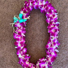 Purple and white orchid lei with a turquoise ribbon bow