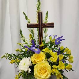 Yellow roses and purple flowers arranged around a wooden cross
