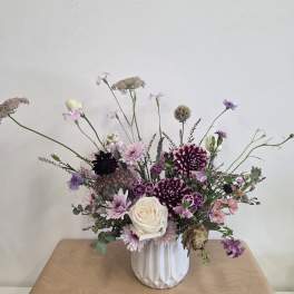Mixed purple and white floral arrangement in a white vase