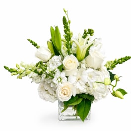 White floral arrangement in a clear square vase with lilies, roses, and hydrangeas