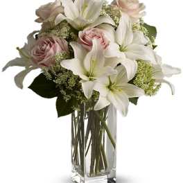 White lilies and pale pink roses arranged in a clear glass vase
