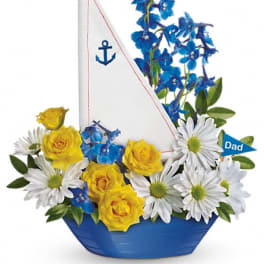 Blue and yellow floral arrangement in a boat-shaped container with a sail