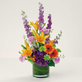 Colorful bouquet with lilies, gerbera daisies, and purple blooms in a glass vase