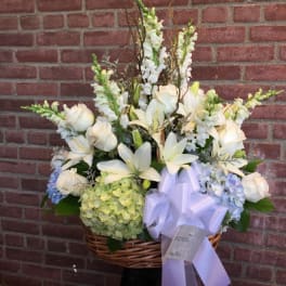 White floral arrangement in a wicker basket with a lavender ribbon