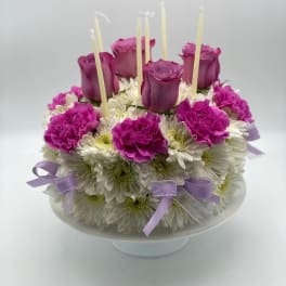 Round floral cake with purple roses and white daisies on a pedestal stand
