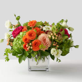 Mixed bouquet of orange, pink, and white roses in a clear glass vase