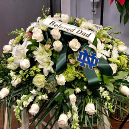 White floral funeral spray with a "Beloved Dad" ribbon and Notre Dame emblem