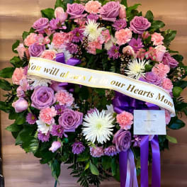 Heart-shaped floral wreath with purple and pink flowers and a memorial ribbon